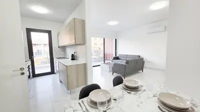 a white living room with a table and a kitchen at Poolside Lux Apartment in Larnaka