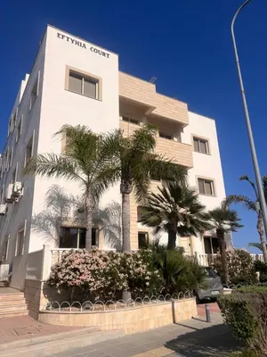 a white building with palm trees in front of it at Sandy Kisses in Larnaka
