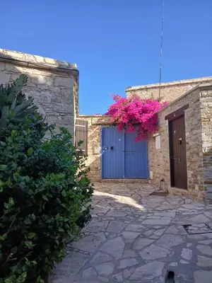 a stone building with a blue door and pink flowers at Hillside Cozy Apartment in Skarinou