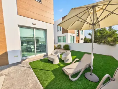 a patio with a lawn with chairs and an umbrella at Alassia Blue Villa in Protaras