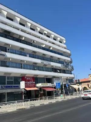 a white car driving past a large building at El Giorgios City Centre Apartment in Larnaka