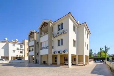 a large white building with cars parked in a parking lot at Nautical Club Penthouse Apartments in Larnaka