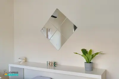 a mirror on a wall above a white shelf at Dios Ponte 102 Beachfront in Larnaka
