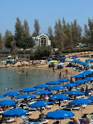 a beach with blue umbrellas and people in the water at Sunny Escape, Protaras, Cyprus in Protaras