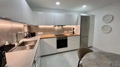 a kitchen with white cabinets and a sink and a table at Kantara Garden Apt by TrulyCyprus in Limassol