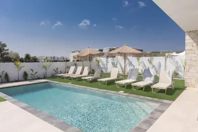 a swimming pool with chairs and umbrellas next to a fence at Ayia Napa Orea Villa OR2 in Ayia Napa