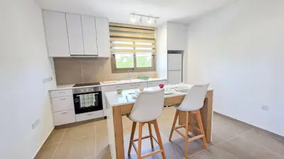 a kitchen with white cabinets and a island with two stools at Olive Dunes Stay in Larnaka