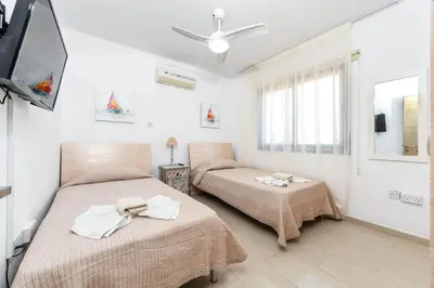 a bedroom with two beds and a tv and a window at Nissi Apartment #102 in Ayia Napa