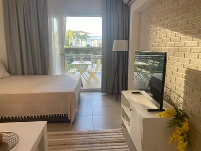 a bedroom with a bed and a tv and a balcony at Family friendly modern flat in Caesar Resort &SPA, Long Beach İSKELE, KKTC in Iskele