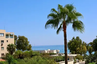 a palm tree in front of a building and the ocean at Beach Front Apartment in Limassol