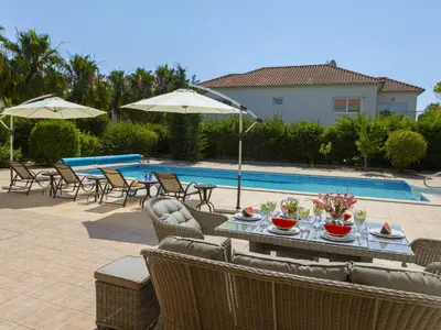 a table with chairs and umbrellas next to a pool at Pervolia Nirides Seaside Mansion 7 in Larnaka