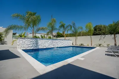 a swimming pool with a stone wall and palm trees at Raise Cityscape Limassol Suites in Limassol