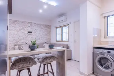 a white kitchen with a table and two stools at Finikoudes gate in Larnaka