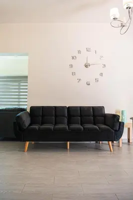 a black couch in a living room with a clock on the wall at Bluewave Apartment in Pyla