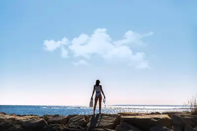 a woman standing on the rocks at the beach at Melon Boutique Seafront Apartment in Limassol