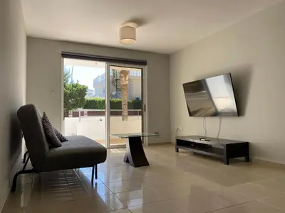 a living room with a chair and a table and a television at Nissi Bliss Apartment in Ayia Napa