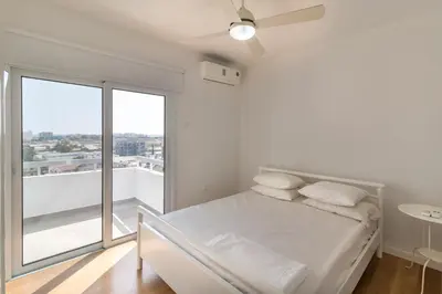 a white bedroom with a bed and a balcony at Limanaki Beach Aparment in Larnaka