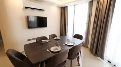 a dining room table with chairs and a television on a wall at Girne Merkezde Geniş Teraslı Havuzlu Daire in Alsancak
