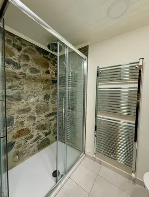 a bathroom with a walk in shower next to a stone wall at To Petrino 4 Studio- Nature, Comfort & Tradition Under One Roof in Kalopanayiotis