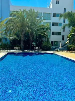 a large swimming pool with palm trees in front of a building at A Home at Coralli - Protaras Beach Apartment, 30 m from beach in Protaras