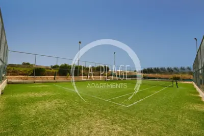 a tennis court with a net on a grass field at Sunny 2Br Family Apartment - Mythical Sands Resort in Protaras