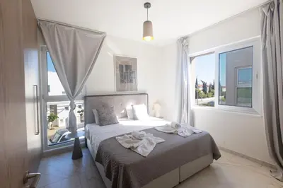 a white bedroom with a bed with a large window at Mythical Blue Villas in Protaras