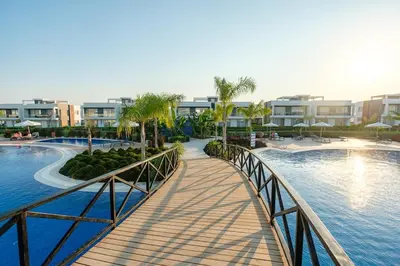 a bridge over a pool with palm trees and buildings at Chic Blue Apartment with Terrace in Paralimni