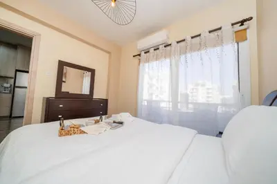 a bedroom with a white bed with a dresser and a window at Seafront 1 bedroom flat in Limassol