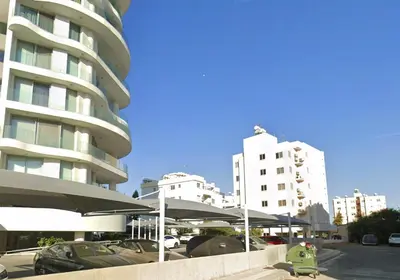 a parking lot with umbrellas in front of a building at Sunset Poolside Apartment with Pool facility in Larnaka