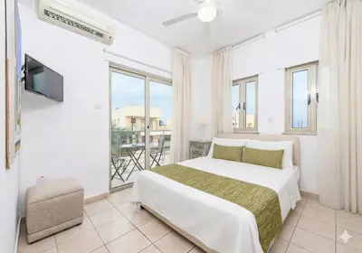 a white bedroom with a bed and a balcony at Fig Tree Beach Villa Five in Protaras