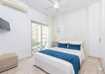 a white bedroom with a bed and a tv at Fig Tree Beach Villa Six in Protaras