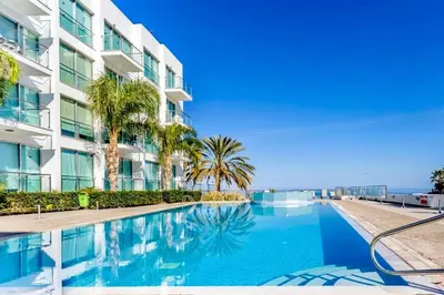 a swimming pool in front of a building with palm trees at Beachfront Seaview Apartment in Paralimni