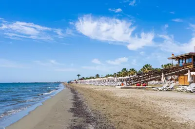 a beach with chairs and umbrellas and the ocean at Compass 1-Bedroom Apartment in Larnaka