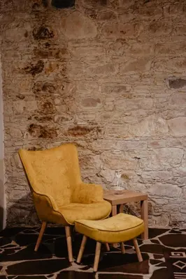 a yellow chair and a stool next to a brick wall at Stonehouse in Monagri