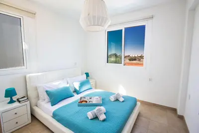 a bedroom with a bed with blue sheets and a window at Seaspray in Protaras