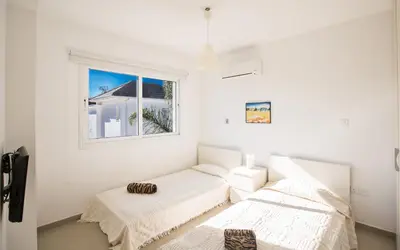 two beds in a white room with a window at Flouressia Villa 4 in Protaras