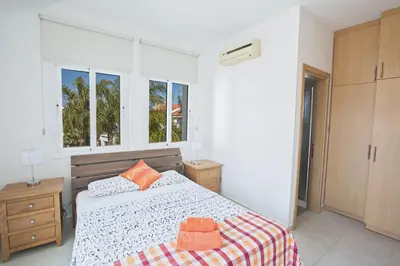 a white bedroom with a bed and two windows at Halle Villa in Protaras