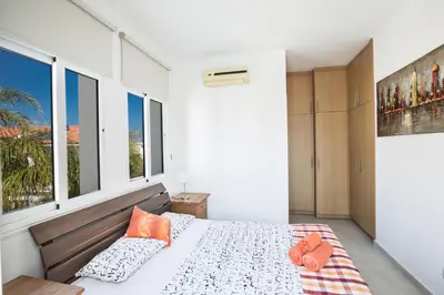 a bedroom with a bed with orange pillows and windows at Halle Villa in Protaras