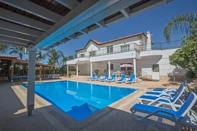 a swimming pool with chairs and a house at Papas Family Villa in Paralimni