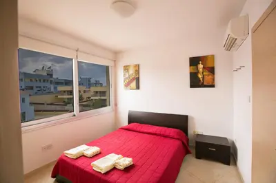 a bedroom with a red bed and a window at Pallinio Fig Tree Bay Apartments in Protaras