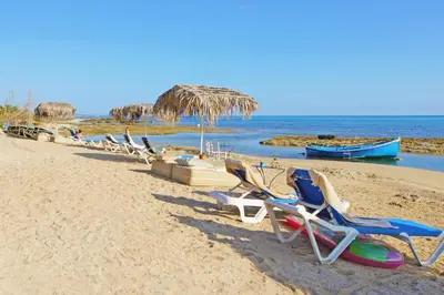 a row of lounge chairs on a beach with a boat at Villa Regina in Ayia Napa