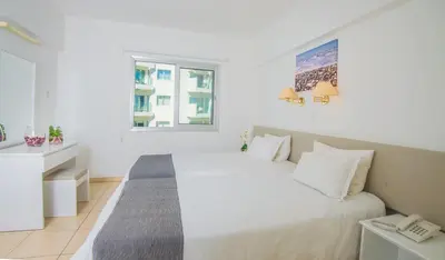 a white bedroom with a bed and a window at Alva Hotel Apartments in Protaras