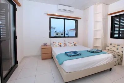a white bedroom with a bed and a window at Green Bay Villa in Protaras