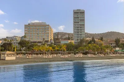 a beach with chaise lounges and chairs and buildings at St Raphael Resort in Limassol