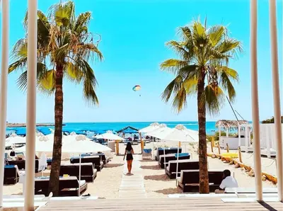 a woman walking along a beach with palm trees at So Nice Beach Resort in Ayia Napa