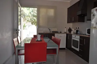 a kitchen with a glass table and red chairs at Sunset Garden Villa in Pervolia