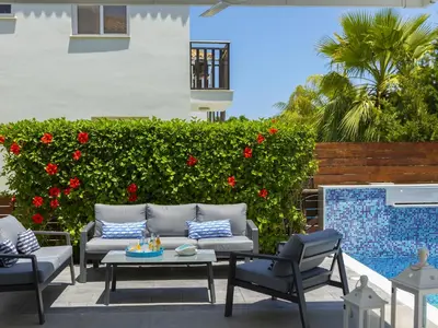 a patio with chairs and a table and red flowers at Passion Villa in Protaras