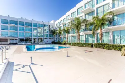 a large apartment building with a swimming pool and palm trees at Coralli Spa By Fig tree Bay in Protaras