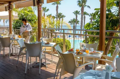 a woman sitting at a restaurant with tables and chairs at Louis Althea Beach in Protaras