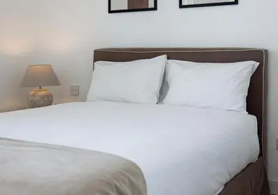 a bed with white sheets and pillows next to a lamp at Nicosia Central Park Residences in Nicosia